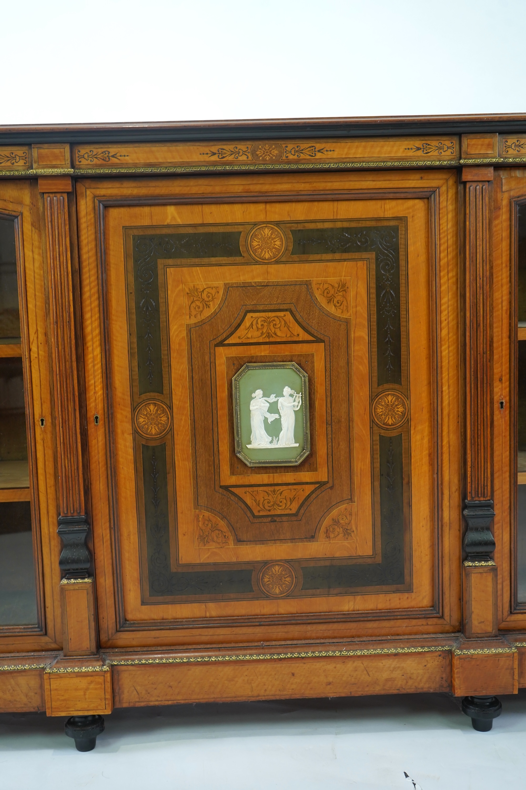 A Victorian marquetry inlaid and gilt metal mounted banded satinwood side cabinet, with anthemion carved frieze over a central door applied octagonal Wedgwood style green and white octagonal jasper plaque, flanked by gla